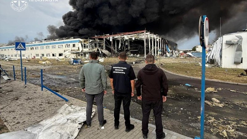 Personel penegak hukum menyaksikan asap mengepul di atas pabrik Flextronics yang terkena serangan rudal Rusia, di tengah serangan Rusia terhadap Ukraina, di Mukachevo, wilayah Zakarpattia, Ukraina, 21 Agustus 2025. (Zakarpattia Regional Prosecutor's Office/Handout via REUTERS)