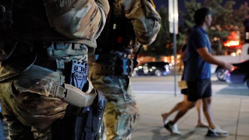Para perempuan bersepeda saat anggota Garda Nasional, yang membawa senjata api berpatroli di National Mall, beberapa minggu setelah Presiden AS Donald Trump memerintahkan Garda Nasional dan penegak hukum untuk berpatroli di ibu kota negara guna membantu pencegahan kejahatan, di Washington, D.C., AS, 26 Agustus 2025. (REUTERS/Jose Luis Gonzalez)