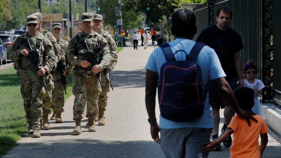 Para perempuan bersepeda saat anggota Garda Nasional, yang membawa senjata api berpatroli di National Mall, beberapa minggu setelah Presiden AS Donald Trump memerintahkan Garda Nasional dan penegak hukum untuk berpatroli di ibu kota negara guna membantu pencegahan kejahatan, di Washington, D.C., AS, 26 Agustus 2025. (REUTERS/Jose Luis Gonzalez)