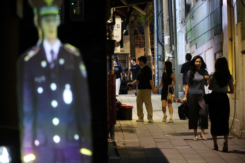 SOUTHKOREA-SECURITY/HOLOGRAM POLICE People walk near a life-size holographic police officer installed to prevent crime at a park in Seoul, South Korea, August 28, 2025. REUTERS/Kim Hong-Ji
