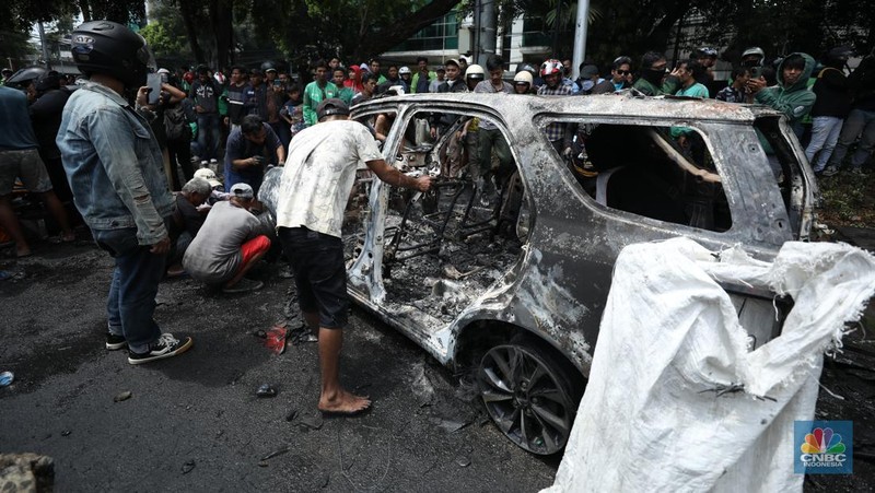 Warga mengambil sisa-sisa besi dari mobil yang hangus terbakar saat aksi di kawasan Mako Brimob Kwitang, Jakarta, Jumat (29/8/2025). (CNBC Indonesia/Tri Susilo)