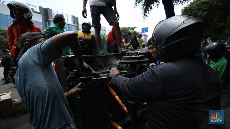 Warga mengambil sisa-sisa besi dari mobil yang hangus terbakar saat aksi di kawasan Mako Brimob Kwitang, Jakarta, Jumat (29/8/2025). (CNBC Indonesia/Tri Susilo)