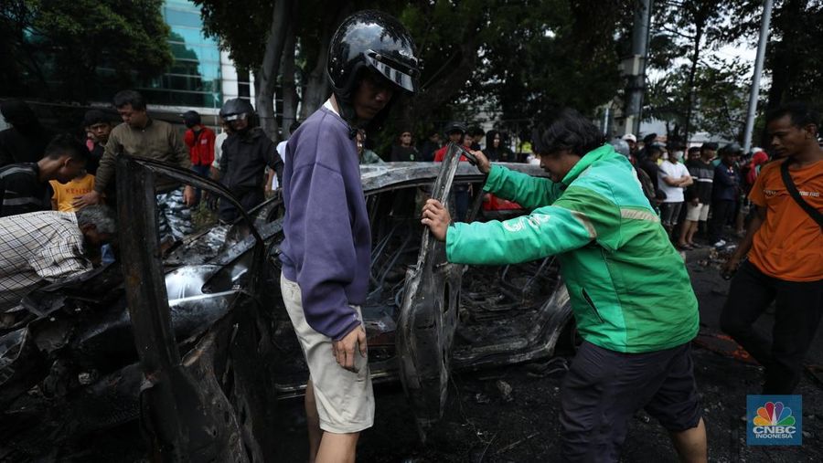 Warga mengambil sisa-sisa besi dari mobil yang hangus terbakar saat aksi di kawasan Mako Brimob Kwitang, Jakarta, Jumat (29/8/2025). (CNBC Indonesia/Tri Susilo)