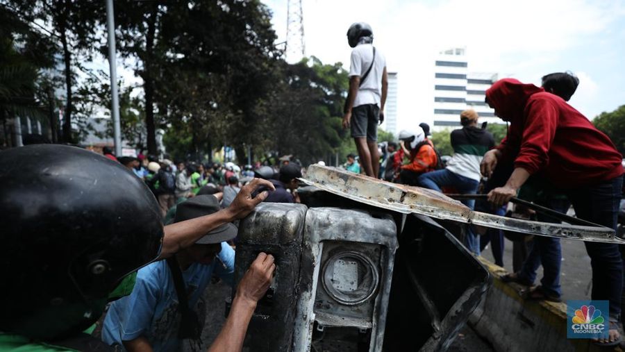 Warga mengambil sisa-sisa besi dari mobil yang hangus terbakar saat aksi di kawasan Mako Brimob Kwitang, Jakarta, Jumat (29/8/2025). (CNBC Indonesia/Tri Susilo)
