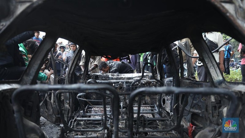 Warga mengambil sisa-sisa besi dari mobil yang hangus terbakar saat aksi di kawasan Mako Brimob Kwitang, Jakarta, Jumat (29/8/2025). (CNBC Indonesia/Tri Susilo)