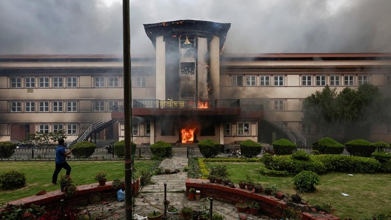 Para demonstran bereaksi di dekat asap yang mengepul dari kompleks Parlemen menyusul kebakaran yang terjadi selama protes terhadap tewasnya 19 orang pada hari Senin setelah protes antikorupsi yang dipicu oleh larangan media sosial, yang kemudian dicabut, selama jam malam di Kathmandu, Nepal, 9 September 2025. (REUTERS/Adnan Abidi)