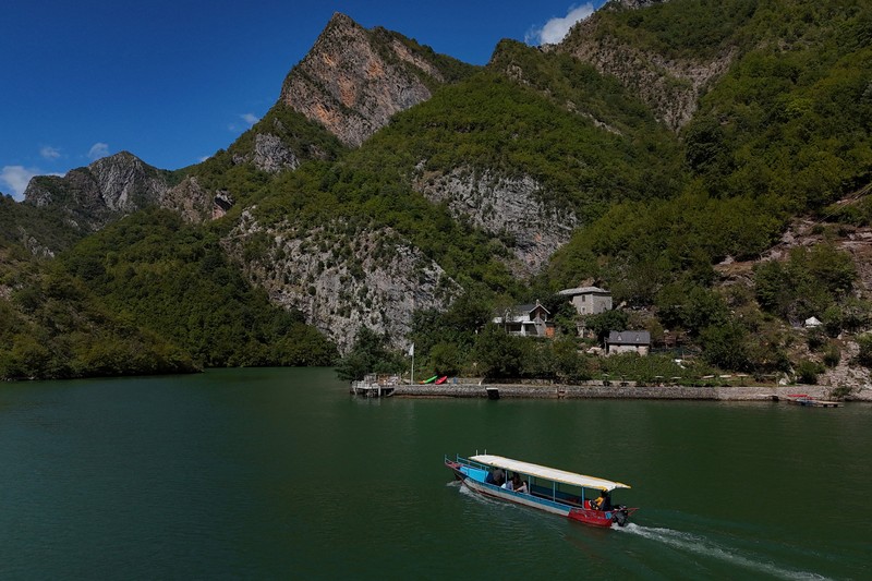 ALBANIA-POLITICS/ A drone view shows a boat carrying tourists near the stone house of Marjana Koceku, 24, a newly elected MP, transformed into an agritourism guesthouse in a remote area at Koman lake near Shkodra, Albania, August 31, 2025. REUTERS/Florion Goga