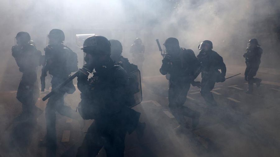 French riot police stand amid tear gas during clashes at a demonstration in Paris as part of a day of nationwide strikes and protests against the government and cuts in the next budget, with supporters of the 