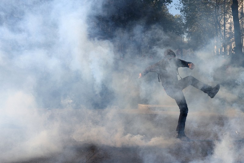 French riot police stand amid tear gas during clashes at a demonstration in Paris as part of a day of nationwide strikes and protests against the government and cuts in the next budget, with supporters of the 