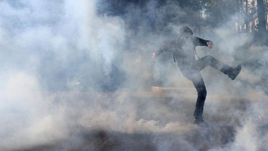 French riot police stand amid tear gas during clashes at a demonstration in Paris as part of a day of nationwide strikes and protests against the government and cuts in the next budget, with supporters of the 
