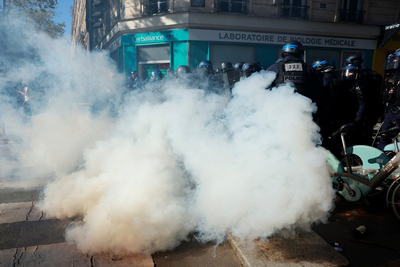 French riot police stand amid tear gas during clashes at a demonstration in Paris as part of a day of nationwide strikes and protests against the government and cuts in the next budget, with supporters of the 