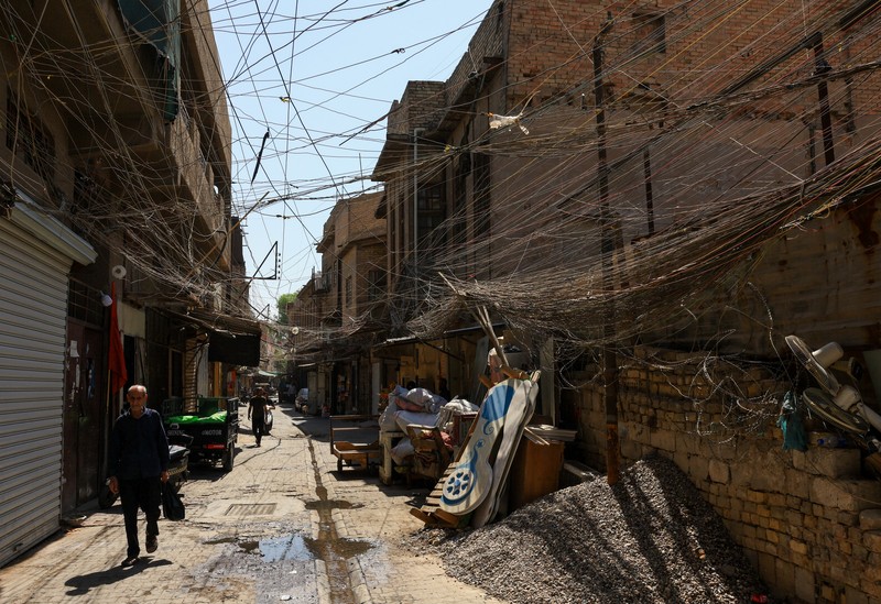 Orang-orang berjalan di sepanjang jalan tua sementara jalinan kabel listrik yang kusut dari generator yang memasok listrik ke rumah-rumah tergantung di atas gedung-gedung, di Baghdad, Irak, 10 September 2025. Orang-orang berjalan di sepanjang jalan tua sementara jalinan kabel listrik yang kusut dari generator yang memasok listrik ke rumah-rumah tergantung di atas gedung-gedung, di Baghdad, Irak, 10 September 2025. (REUTERS/Thaier Al-Sudani)