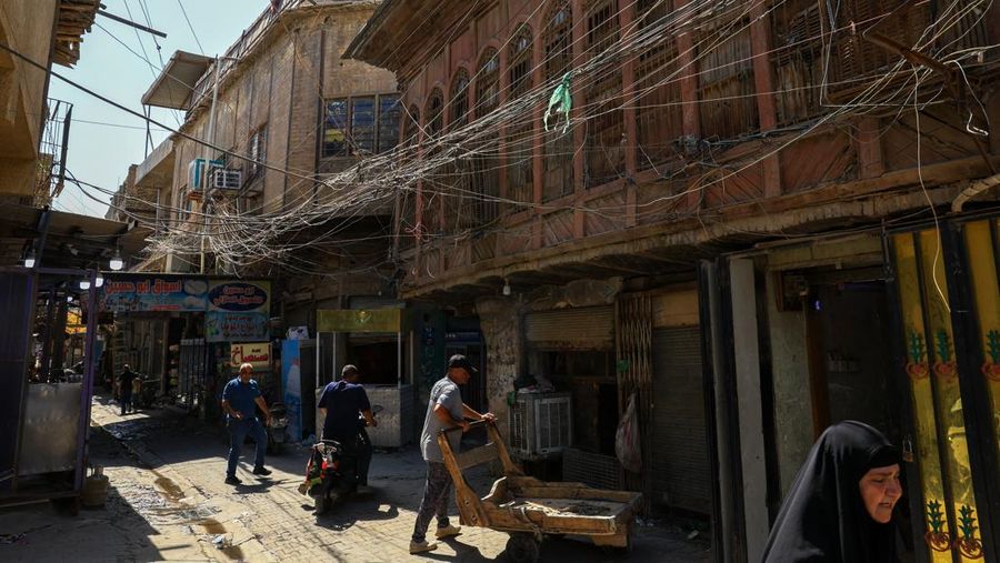 Orang-orang berjalan di sepanjang jalan tua sementara jalinan kabel listrik yang kusut dari generator yang memasok listrik ke rumah-rumah tergantung di atas gedung-gedung, di Baghdad, Irak, 10 September 2025. Orang-orang berjalan di sepanjang jalan tua sementara jalinan kabel listrik yang kusut dari generator yang memasok listrik ke rumah-rumah tergantung di atas gedung-gedung, di Baghdad, Irak, 10 September 2025. (REUTERS/Thaier Al-Sudani)