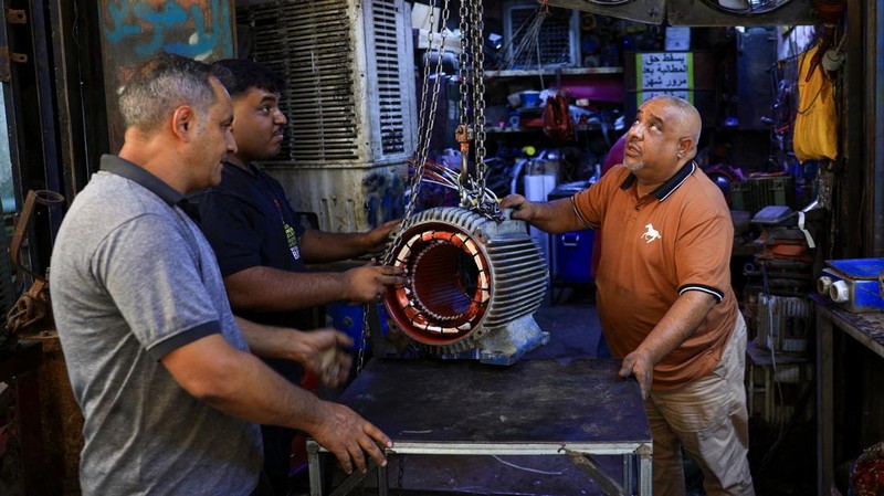 Orang-orang berjalan di sepanjang jalan tua sementara jalinan kabel listrik yang kusut dari generator yang memasok listrik ke rumah-rumah tergantung di atas gedung-gedung, di Baghdad, Irak, 10 September 2025. (REUTERS/Thaier Al-Sudani)