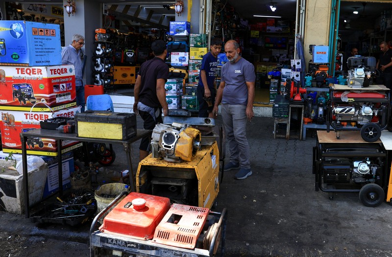 Orang-orang berjalan di sepanjang jalan tua sementara jalinan kabel listrik yang kusut dari generator yang memasok listrik ke rumah-rumah tergantung di atas gedung-gedung, di Baghdad, Irak, 10 September 2025. (REUTERS/Thaier Al-Sudani)