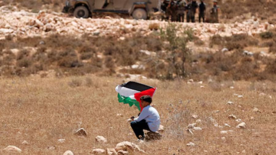 Seorang anak laki-laki memegang bendera Palestina dalam demonstrasi menentang apa yang disebut warga Palestina sebagai perampasan tanah mereka oleh Israel, sementara pasukan keamanan Israel berjaga-jaga, di Raba, dekat Jenin, Tepi Barat yang diduduki Israel, 18 Juli 2025. (REUTERS/Raneen Sawafta/File Photo)