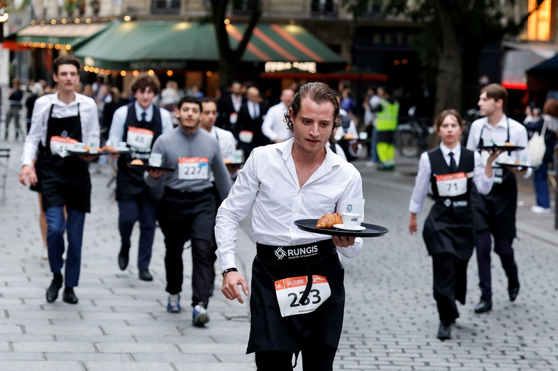 Pelayan membawa nampan berisi secangkir kopi, croissant, dan segelas air ikut serta dalam Cafe Race di Paris, Prancis, 21 September 2025. (REUTERS/Stephanie Lecocq)