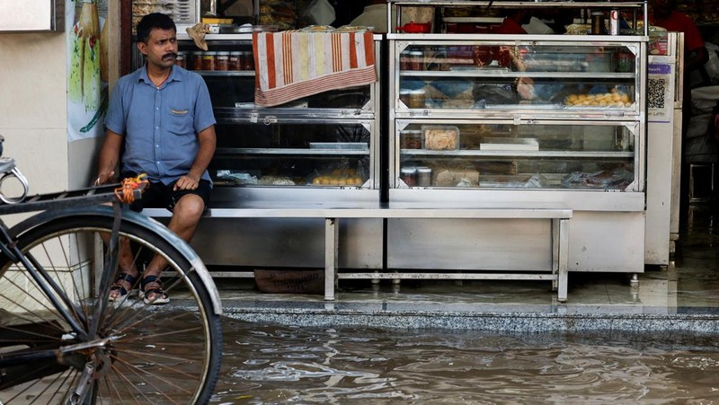Orang-orang berjalan melalui jalan yang tergenang air setelah hujan deras di Kolkata, India, 24 September 2025. (REUTERS/Sahiba Chawdhary)