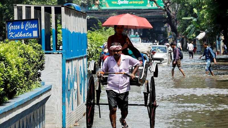 Orang-orang berjalan melalui jalan yang tergenang air setelah hujan deras di Kolkata, India, 24 September 2025. (REUTERS/Sahiba Chawdhary)