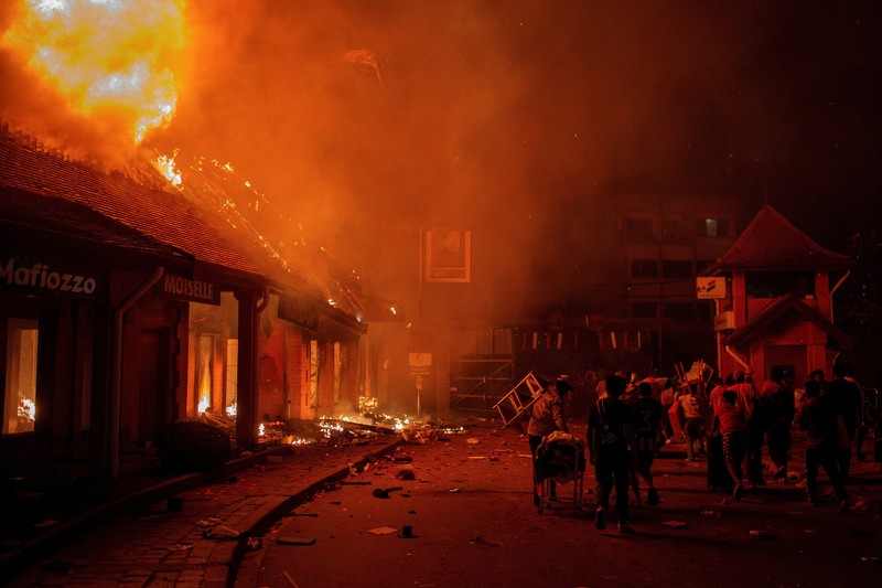 Para pekerja menyelamatkan barang-barang mereka dari toko yang terbakar selama demonstrasi untuk mengecam seringnya pemadaman listrik dan kekurangan air di Antananarivo, Madagaskar, 25 September 2025. (REUTERS/Zo Andrianjafy)