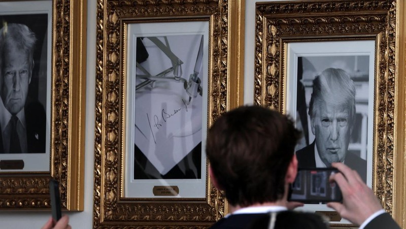 Journalists take pictures of an image of an autopen signing former U.S. President Joe Biden's signature which is displayed in place of a portrait of Biden next to portraits of U.S President Donald Trump at the 
