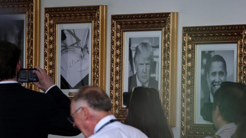 Journalists take pictures of an image of an autopen signing former U.S. President Joe Biden's signature which is displayed in place of a portrait of Biden next to portraits of U.S President Donald Trump at the 