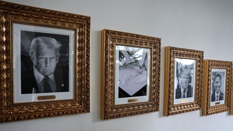 Journalists take pictures of an image of an autopen signing former U.S. President Joe Biden's signature which is displayed in place of a portrait of Biden next to portraits of U.S President Donald Trump at the 