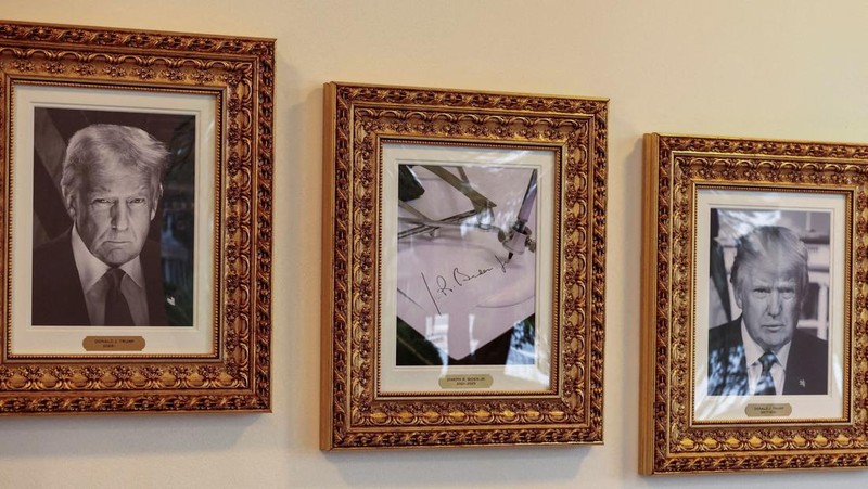 Journalists take pictures of an image of an autopen signing former U.S. President Joe Biden's signature which is displayed in place of a portrait of Biden next to portraits of U.S President Donald Trump at the 