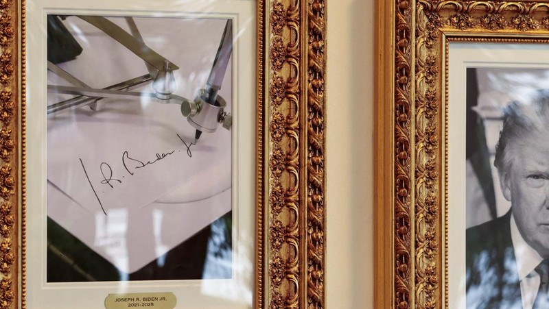 Journalists take pictures of an image of an autopen signing former U.S. President Joe Biden's signature which is displayed in place of a portrait of Biden next to portraits of U.S President Donald Trump at the 