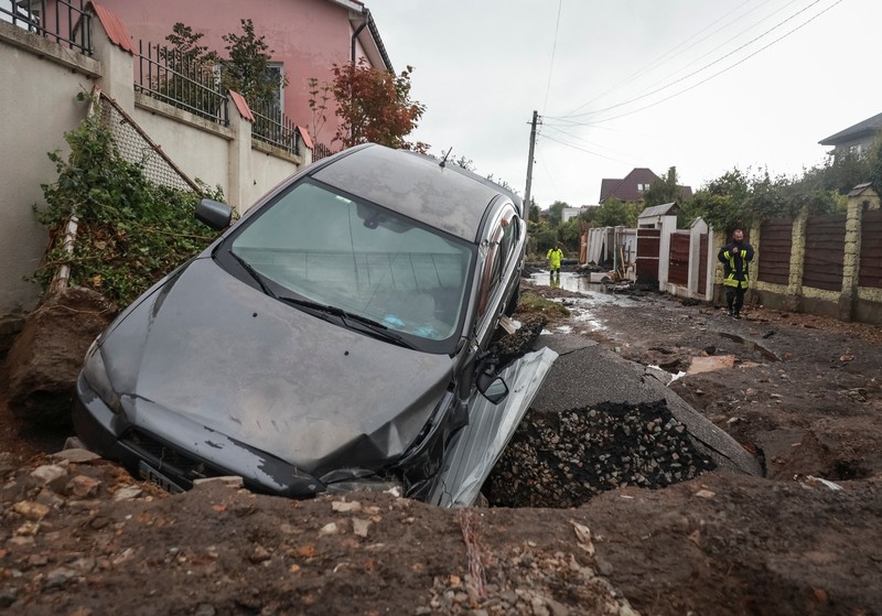 Sebuah bus dan mobil terjebak di lubang besar yang terbuka di jalan, setelah hujan lebat yang belum pernah terjadi sebelumnya di Odesa, Ukraina, Rabu (1/10/2025). (REUTERS/Nina Liashonok)