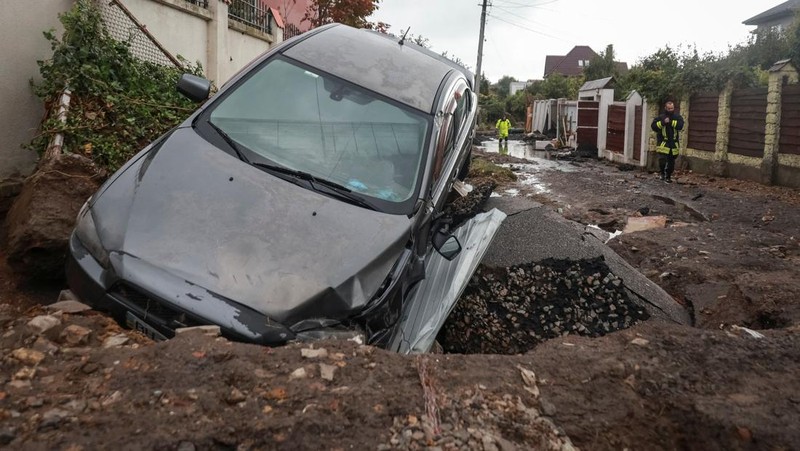 Sebuah bus dan mobil terjebak di lubang besar yang terbuka di jalan, setelah hujan lebat yang belum pernah terjadi sebelumnya di Odesa, Ukraina, Rabu (1/10/2025). (REUTERS/Nina Liashonok)