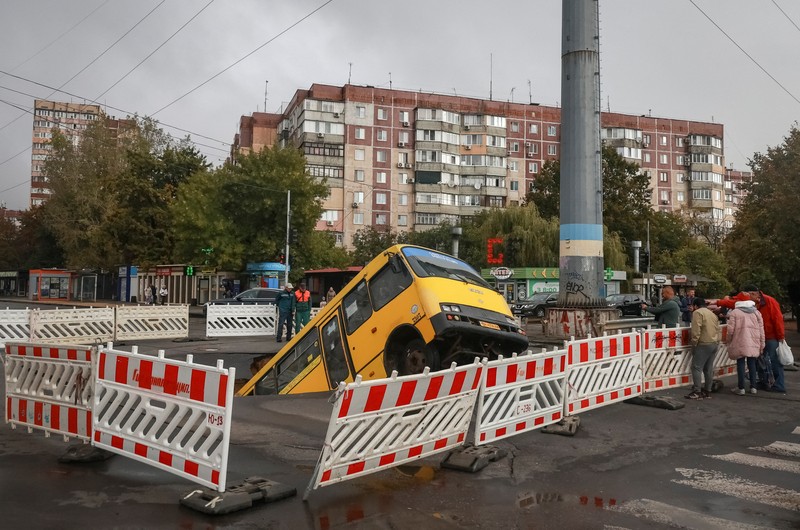 Sebuah bus dan mobil terjebak di lubang besar yang terbuka di jalan, setelah hujan lebat yang belum pernah terjadi sebelumnya di Odesa, Ukraina, Rabu (1/10/2025). (REUTERS/Nina Liashonok)