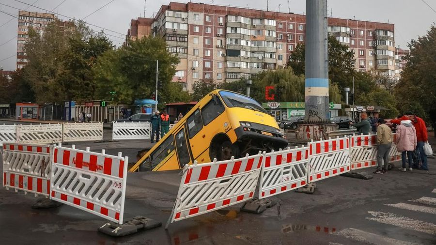 Sebuah bus dan mobil terjebak di lubang besar yang terbuka di jalan, setelah hujan lebat yang belum pernah terjadi sebelumnya di Odesa, Ukraina, Rabu (1/10/2025). (REUTERS/Nina Liashonok)