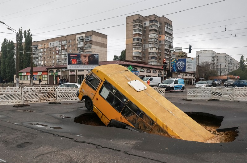Sebuah bus dan mobil terjebak di lubang besar yang terbuka di jalan, setelah hujan lebat yang belum pernah terjadi sebelumnya di Odesa, Ukraina, Rabu (1/10/2025). (REUTERS/Nina Liashonok)