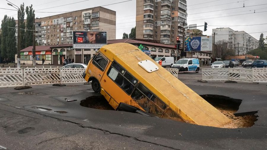 Sebuah bus dan mobil terjebak di lubang besar yang terbuka di jalan, setelah hujan lebat yang belum pernah terjadi sebelumnya di Odesa, Ukraina, Rabu (1/10/2025). (REUTERS/Nina Liashonok)