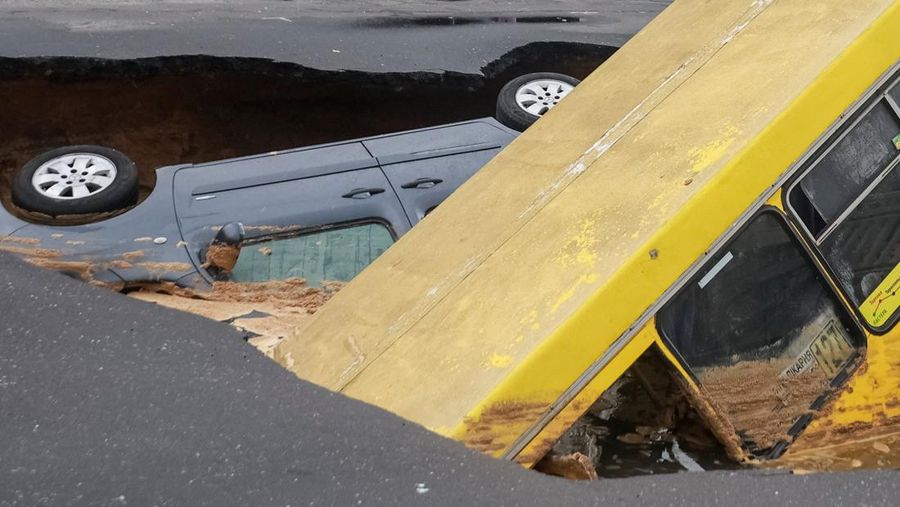Sebuah bus dan mobil terjebak di lubang besar yang terbuka di jalan, setelah hujan lebat yang belum pernah terjadi sebelumnya di Odesa, Ukraina, Rabu (1/10/2025). (REUTERS/Nina Liashonok)