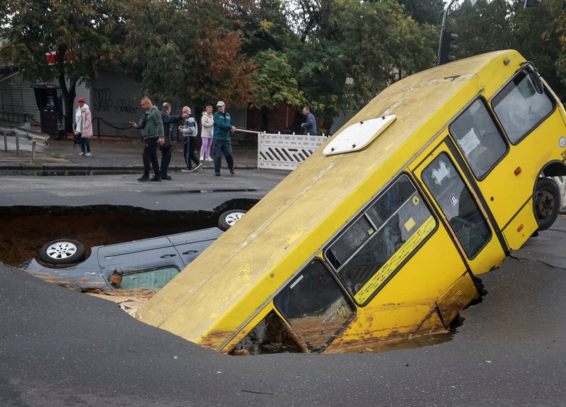 Sebuah bus dan mobil terjebak di lubang besar yang terbuka di jalan, setelah hujan lebat yang belum pernah terjadi sebelumnya di Odesa, Ukraina, Rabu (1/10/2025). (REUTERS/Nina Liashonok)