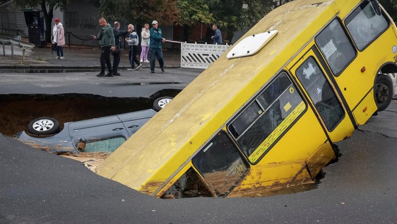 Sebuah bus dan mobil terjebak di lubang besar yang terbuka di jalan, setelah hujan lebat yang belum pernah terjadi sebelumnya di Odesa, Ukraina, Rabu (1/10/2025). (REUTERS/Nina Liashonok)