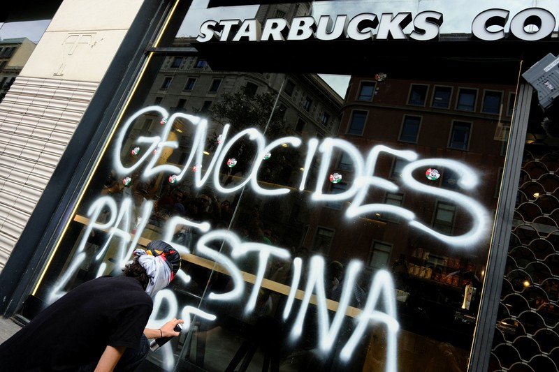 Seorang mahasiswa berunjuk rasa di depan kedai kopi Starbucks selama protes pro-Palestina untuk mengutuk intersepsi pasukan Israel terhadap kapal-kapal Armada Global Sumud yang bertujuan mencapai Gaza dan menerobos blokade laut Israel, di Barcelona, Spanyol, 2 Oktober 2025. Seorang mahasiswa berunjuk rasa di depan kedai kopi Starbucks selama protes pro-Palestina untuk mengutuk intersepsi pasukan Israel terhadap kapal-kapal Armada Global Sumud yang bertujuan mencapai Gaza dan menerobos blokade laut Israel, di Barcelona, Spanyol, 2 Oktober 2025. (REUTERS/Nacho Doce)