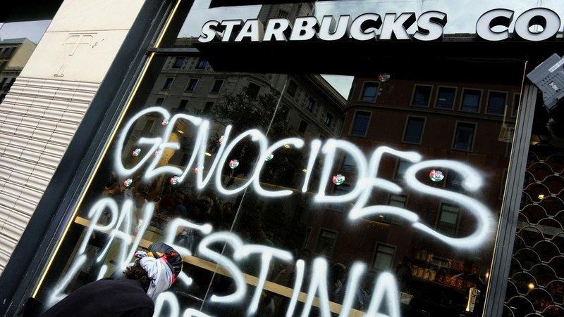 Seorang mahasiswa berunjuk rasa di depan kedai kopi Starbucks selama protes pro-Palestina untuk mengutuk intersepsi pasukan Israel terhadap kapal-kapal Armada Global Sumud yang bertujuan mencapai Gaza dan menerobos blokade laut Israel, di Barcelona, ​​Spanyol, 2 Oktober 2025. (REUTERS/Nacho Doce)