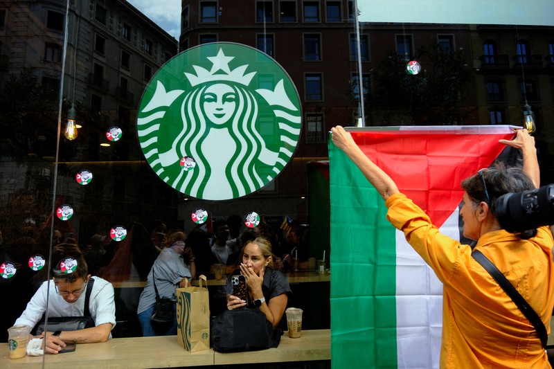 Seorang mahasiswa berunjuk rasa di depan kedai kopi Starbucks selama protes pro-Palestina untuk mengutuk intersepsi pasukan Israel terhadap kapal-kapal Armada Global Sumud yang bertujuan mencapai Gaza dan menerobos blokade laut Israel, di Barcelona, ​​Spanyol, 2 Oktober 2025. (REUTERS/Nacho Doce)