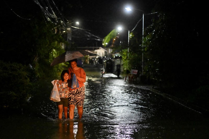 Seorang wanita berjalan melewati jalan yang banjir setelah hujan, yang diperparah oleh Badai Tropis Matmo, di Santa Lucia, Calumpit, provinsi Bulacan, Filipina, 3 Oktober 2025. (REUTERS/Noel Celis)
