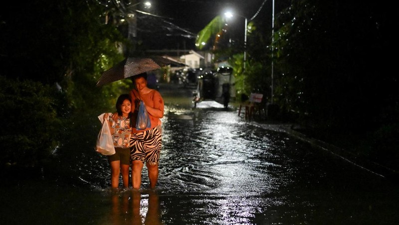 Seorang wanita berjalan melewati jalan yang banjir setelah hujan, yang diperparah oleh Badai Tropis Matmo, di Santa Lucia, Calumpit, provinsi Bulacan, Filipina, 3 Oktober 2025. (REUTERS/Noel Celis)
