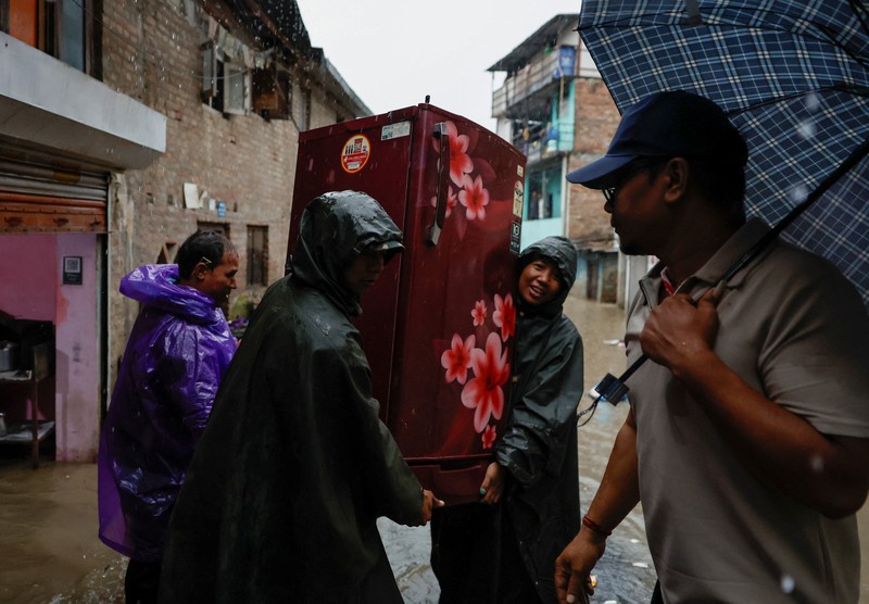 Seorang pria membawa payung berjalan melewati grafiti bertuliskan 'Nepal' di jalan yang banjir di sepanjang tepi Sungai Bagmati yang meluap setelah hujan lebat, di Kathmandu, Nepal, 4 Oktober 2025. (REUTERS/Navesh Chitrakar)