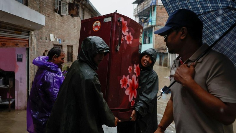 Seorang pria membawa payung berjalan melewati grafiti bertuliskan 'Nepal' di jalan yang banjir di sepanjang tepi Sungai Bagmati yang meluap setelah hujan lebat, di Kathmandu, Nepal, 4 Oktober 2025. (REUTERS/Navesh Chitrakar)