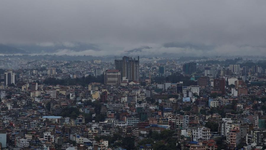 Seorang pria membawa payung berjalan melewati grafiti bertuliskan 'Nepal' di jalan yang banjir di sepanjang tepi Sungai Bagmati yang meluap setelah hujan lebat, di Kathmandu, Nepal, 4 Oktober 2025. (REUTERS/Navesh Chitrakar)