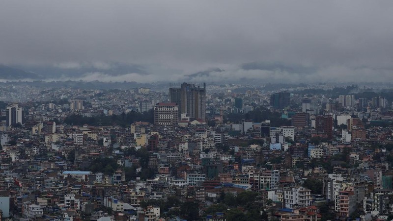 Seorang pria membawa payung berjalan melewati grafiti bertuliskan 'Nepal' di jalan yang banjir di sepanjang tepi Sungai Bagmati yang meluap setelah hujan lebat, di Kathmandu, Nepal, 4 Oktober 2025. (REUTERS/Navesh Chitrakar)