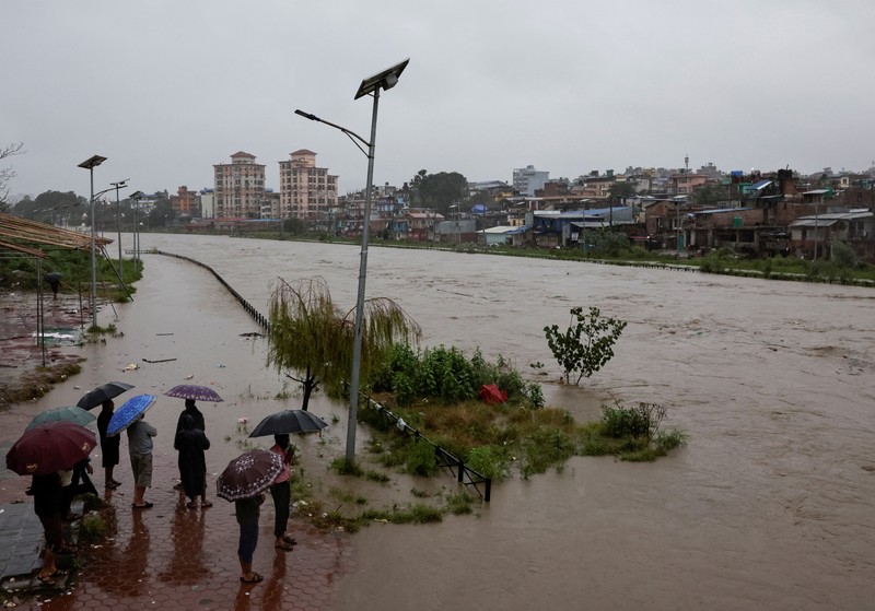 Seorang pria membawa payung berjalan melewati grafiti bertuliskan 'Nepal' di jalan yang banjir di sepanjang tepi Sungai Bagmati yang meluap setelah hujan lebat, di Kathmandu, Nepal, 4 Oktober 2025. (REUTERS/Navesh Chitrakar)