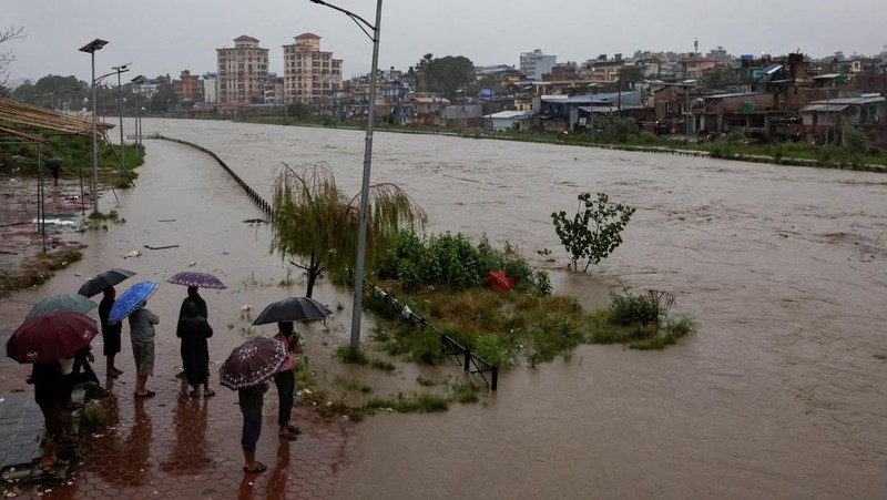Seorang pria membawa payung berjalan melewati grafiti bertuliskan 'Nepal' di jalan yang banjir di sepanjang tepi Sungai Bagmati yang meluap setelah hujan lebat, di Kathmandu, Nepal, 4 Oktober 2025. (REUTERS/Navesh Chitrakar)