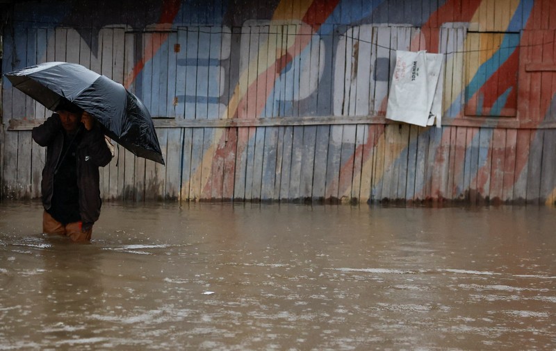 Seorang pria membawa payung berjalan melewati grafiti bertuliskan 'Nepal' di jalan yang banjir di sepanjang tepi Sungai Bagmati yang meluap setelah hujan lebat, di Kathmandu, Nepal, 4 Oktober 2025. (REUTERS/Navesh Chitrakar)